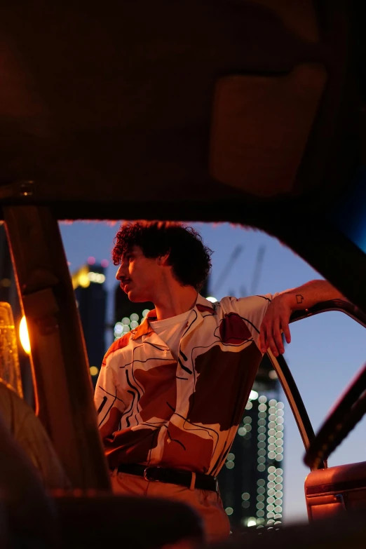 a man sitting in the passenger seat of a car, an album cover, pexels contest winner, standing on rooftop, city hunter, patterned clothing, dusk light