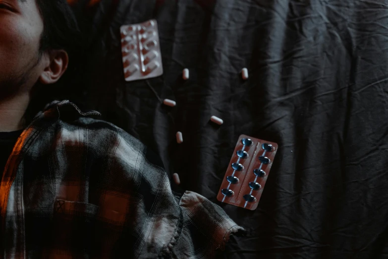 a young boy laying on top of a bed covered in pills, by Elsa Bleda, pexels contest winner, antipodeans, dark and dim, flannel, draped with horrors and spines, a wooden