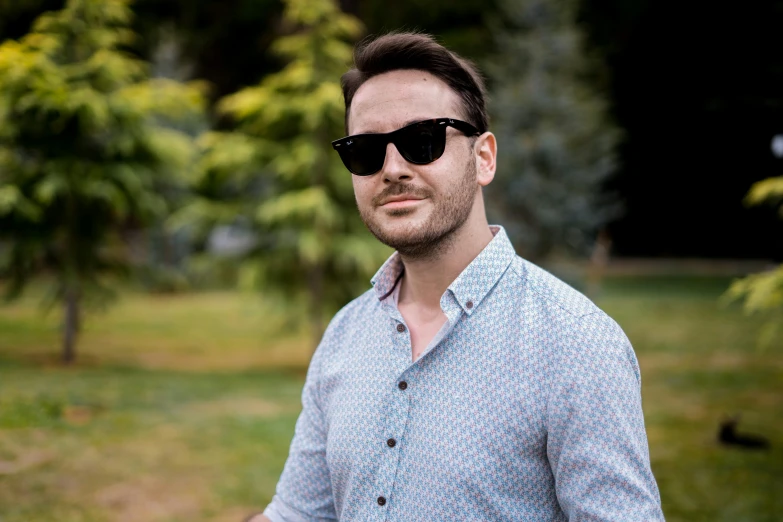 a man wearing sunglasses standing in a park, a portrait, by Adam Marczyński, charlie cox, avatar image, profile image, wearing a shirt