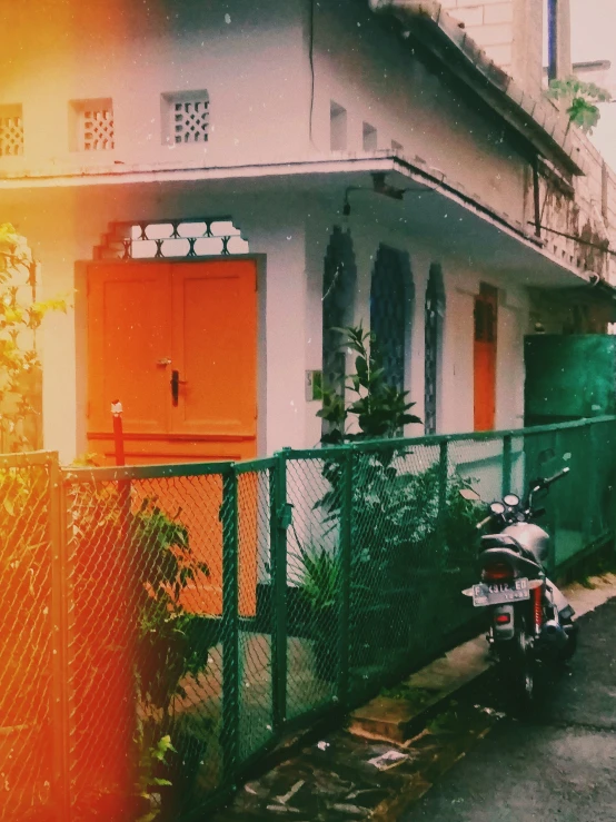 a motorcycle is parked in front of a building, a colorized photo, unsplash, bengal school of art, orange glow, cottage close up, background image