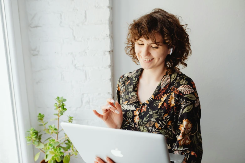 a woman sitting in front of a laptop computer, pexels contest winner, wearing a blouse, profile image, dark short curly hair smiling, delicate patterned