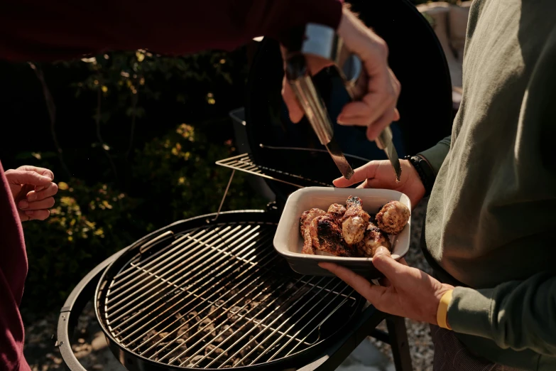 a group of people standing around a grill with food on it, bowl filled with food, shot with sony alpha 1 camera, chicken, close-up imagery