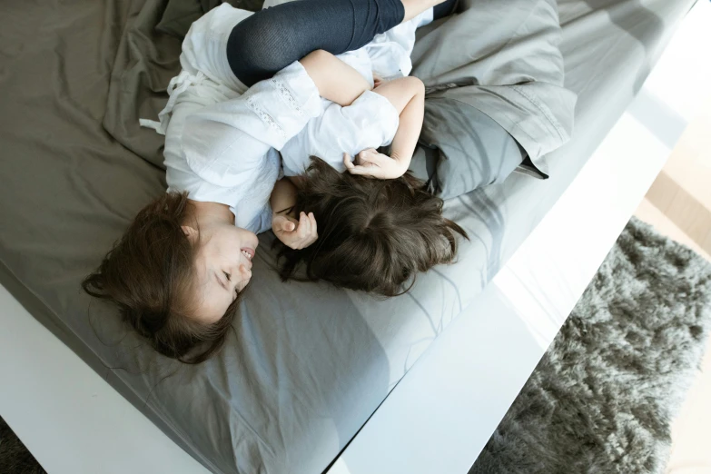 a couple of kids laying on top of a bed, by Emma Andijewska, pexels contest winner, incoherents, woman holding another woman, modern design, brunettes, looking down