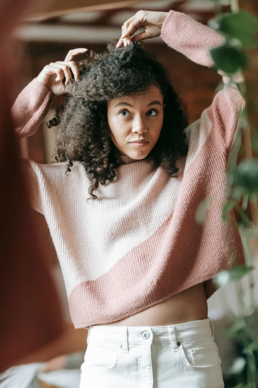 a woman brushing her hair in front of a mirror, by Carey Morris, trending on pexels, renaissance, sweater, brown and pink color scheme, made of wool, mixed race woman