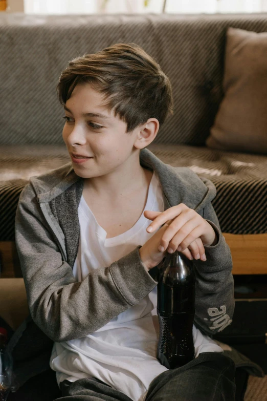 a boy sitting on the floor holding a bottle of beer, pexels contest winner, happening, sitting on a couch, wearing jacket, lachlan bailey, with a bottle of wine