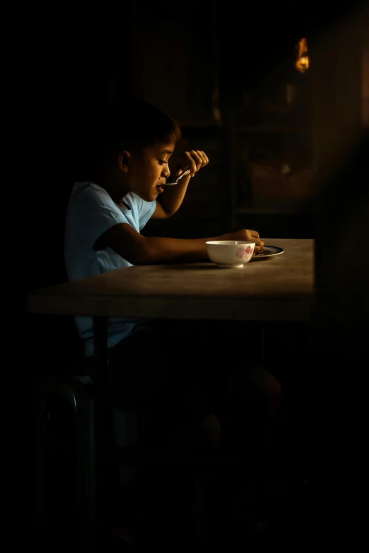 a young boy sitting at a table in the dark, by Lily Delissa Joseph, pexels contest winner, morning sun, rice, medium format. soft light, breakfast