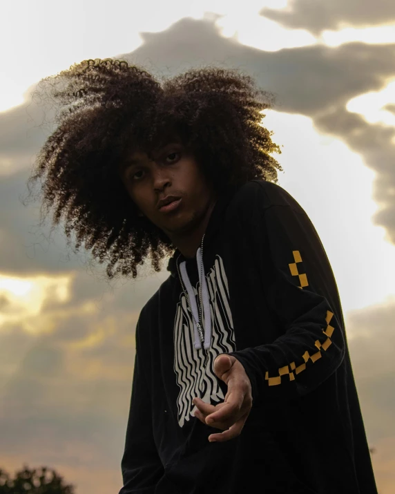 a young man standing on top of a skateboard, an album cover, pexels contest winner, afrofuturism, frizzy hair, looking off into the sunset, black and yellow tracksuit, beautiful androgynous prince