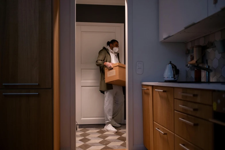 a man standing in a kitchen holding a box, a stock photo, by Eglon van der Neer, pexels contest winner, apartment hallway, good night, masked person in corner, reuniting