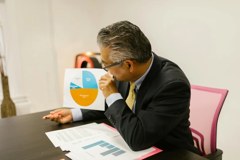 a man sitting at a table holding a piece of paper, infographics, profile image, colour photograph, khyzyl saleem