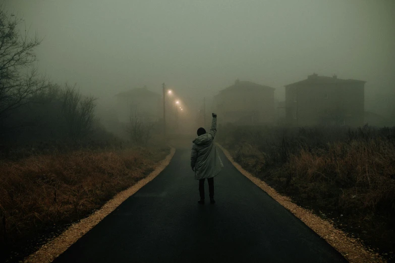 a person walking down a road on a foggy day, by Lucia Peka, pexels contest winner, magical realism, zombie arms out in front, abandoned town, silent hill aesthetic, toxic glowing smog in the sky