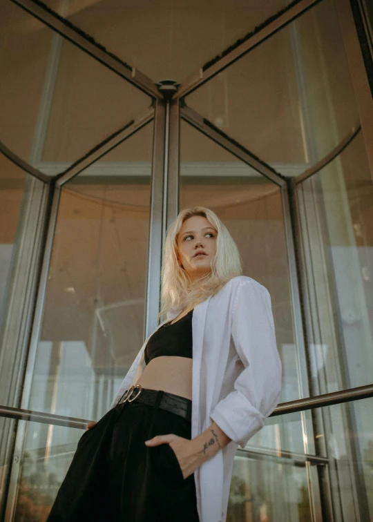 a woman standing in front of a glass building, an album cover, unsplash, albino white pale skin, wearing a crop top, wearing a black jacket, cinematic outfit photo