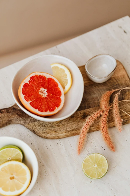 a wooden cutting board topped with slices of grapefruit, a still life, by Carey Morris, trending on pexels, white ceramic shapes, bowl filled with food, botanicals, subtle detailing