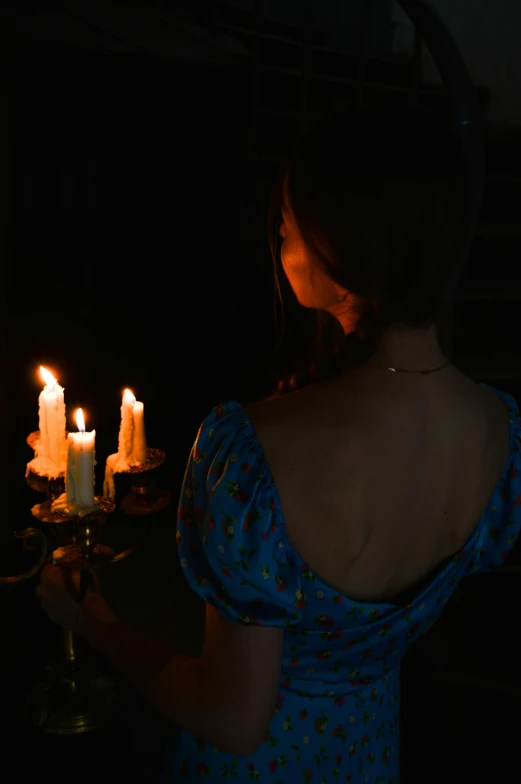 a woman in a blue dress holding a lit candle, inspired by Godfried Schalcken, pexels contest winner, looking across the shoulder, a seance, ( ( theatrical ) ), lit from behind