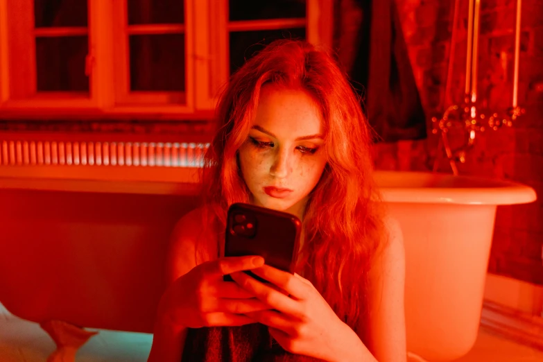 a woman sitting on a bed looking at her cell phone, a portrait, inspired by Elsa Bleda, trending on pexels, renaissance, red neon eyes, redhead girl, orange and red lighting, portrait of kim petras