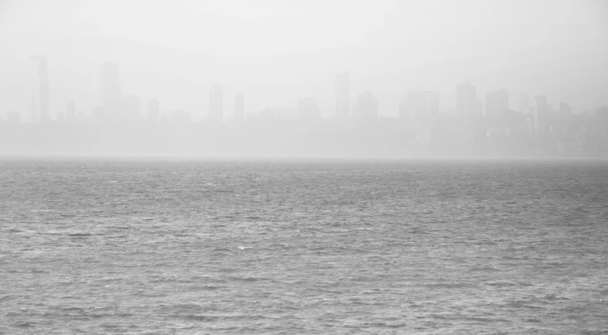 a large body of water with a city in the background, a black and white photo, inspired by Andreas Gursky, pexels, minimalism, in the thick fog, mumbai in the future, soft colors mono chromatic, photo of the middle of the ocean