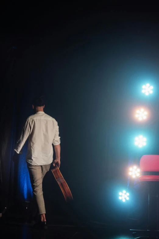 a man standing on a stage holding a skateboard, pexels contest winner, happening, cinemathic lights, walking away from camera, talk show, ( ( theatrical ) )