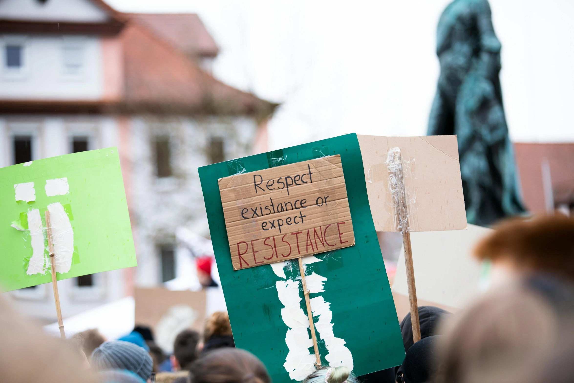 a group of people holding signs in front of a statue, by Julia Pishtar, pexels, a green, resistance, a wooden, february)