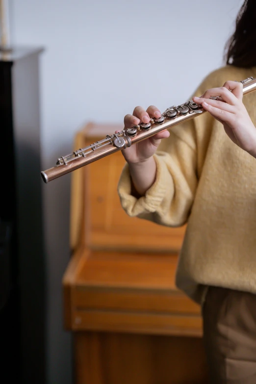 a woman playing a flute in front of a piano, by Matthias Stom, trending on unsplash, hyperrealism, little kid, copper, holding a wood piece, photographed for reuters