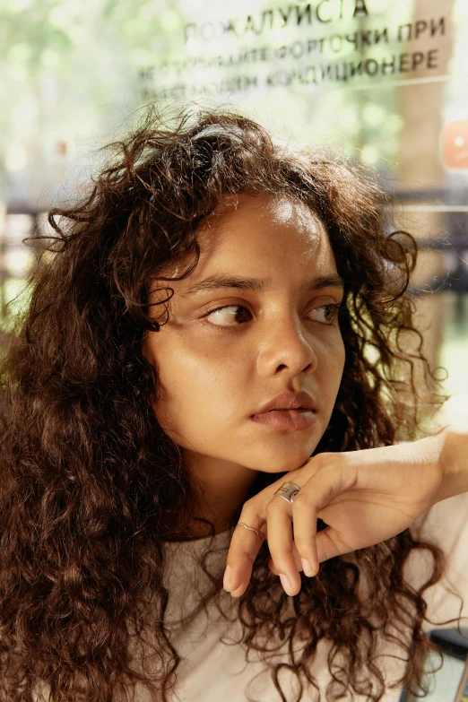 a woman sitting at a table with a plate of food, an album cover, trending on pexels, photorealism, tessa thompson, pensive expression, brown curly hair, dafne keen