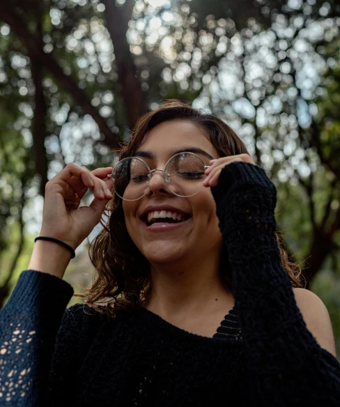 a woman holding a pair of glasses up to her face, by Carey Morris, pexels contest winner, happening, in the park, alanis guillen, smiling young woman, person made out of glass