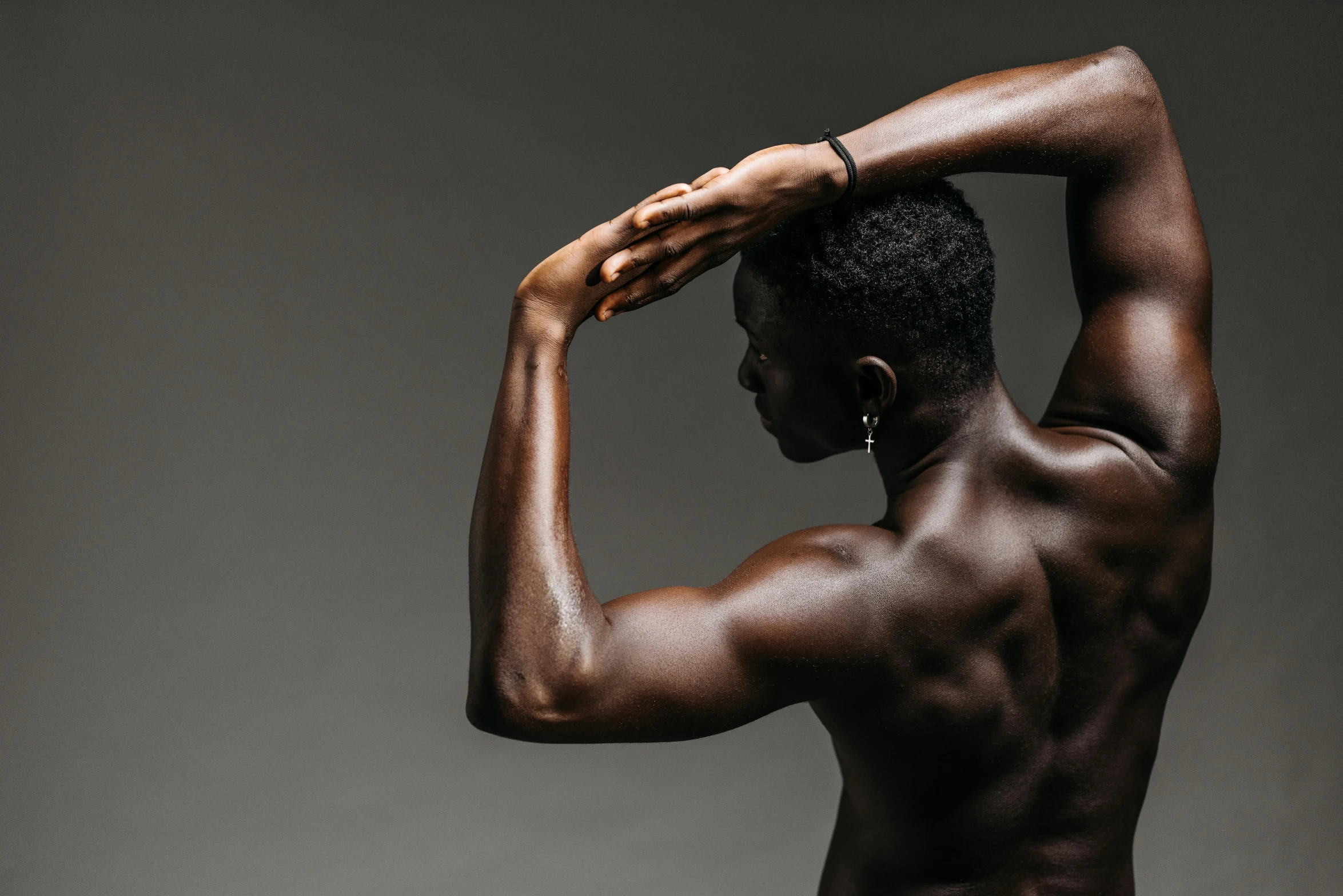 a man that is standing up with his hands on his head, by Carey Morris, pexels contest winner, afrofuturism, bare bodybuilder shoulders. kohl, black human spine, 30 year old man :: athletic, profile pose