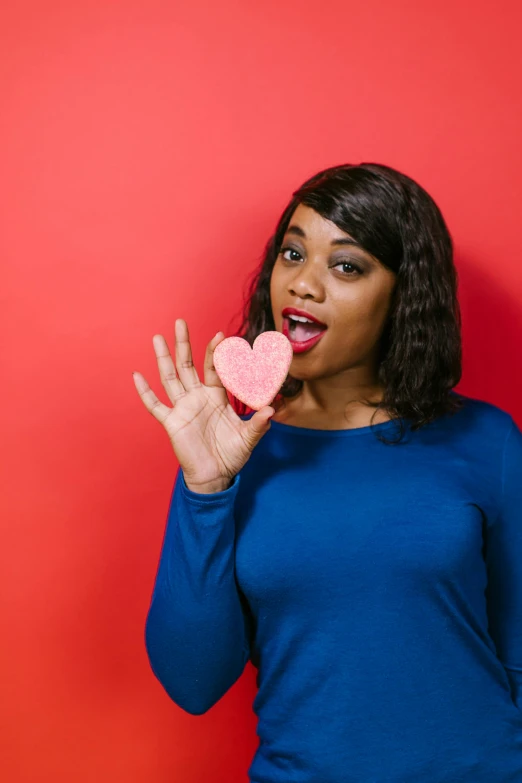 a woman holding a pink heart in front of her face, pexels, happening, photo of a black woman, sarcastic pose, snacks, plain background