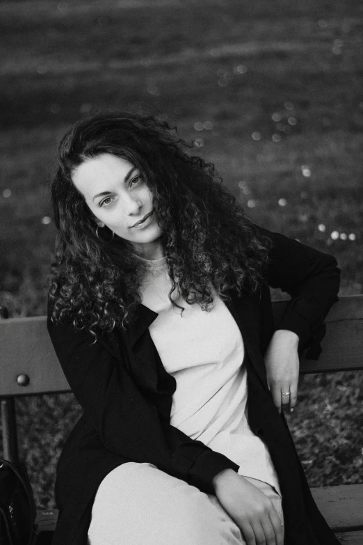 a black and white photo of a woman sitting on a bench, by Lucia Peka, renaissance, curly dark hair, elliot alderson, 30 years old woman, curly