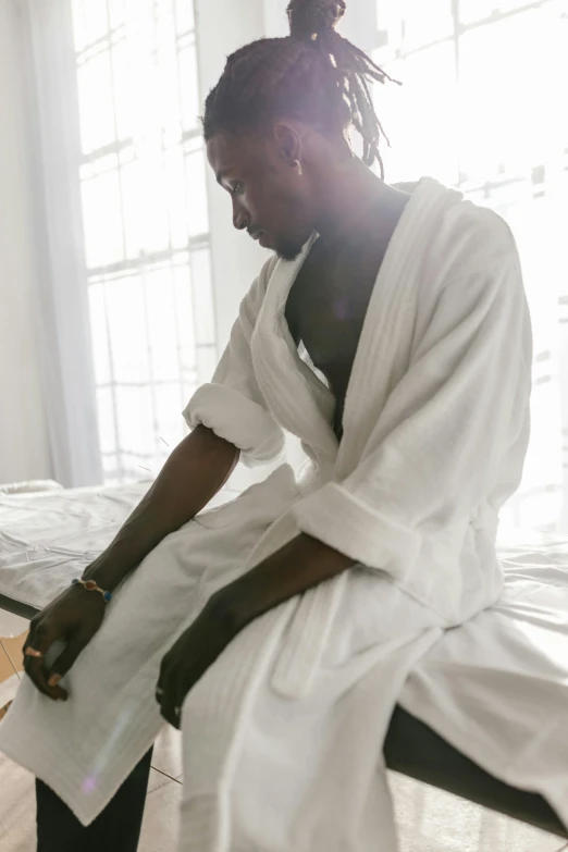 a woman sitting on a bed in a white robe, inspired by Gordon Parks, trending on unsplash, african man, travis scott, wearing a towel, praying posture