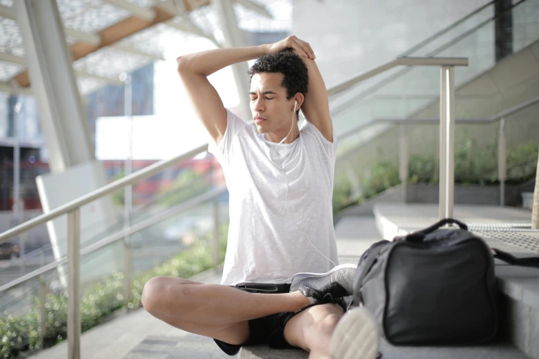 a man sitting on the steps with his hands behind his head, by Carey Morris, pexels contest winner, happening, black. airports, wearing shorts and t shirt, working out, androgynous person