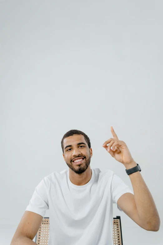 a man in a white shirt sitting in a chair, trending on pexels, 3 5 mm pointing up, grey backdrop, brown skin man with a giant grin, on a white table