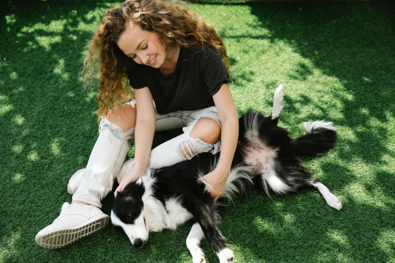 a woman sitting on the ground petting a black and white dog, by Julia Pishtar, aussie, lawn, no cropping, on a canva