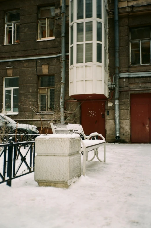 a bench sitting in the snow in front of a building, inspired by Illarion Pryanishnikov, opposite the lift-shaft, tenement buildings, 1997 ), interesting details