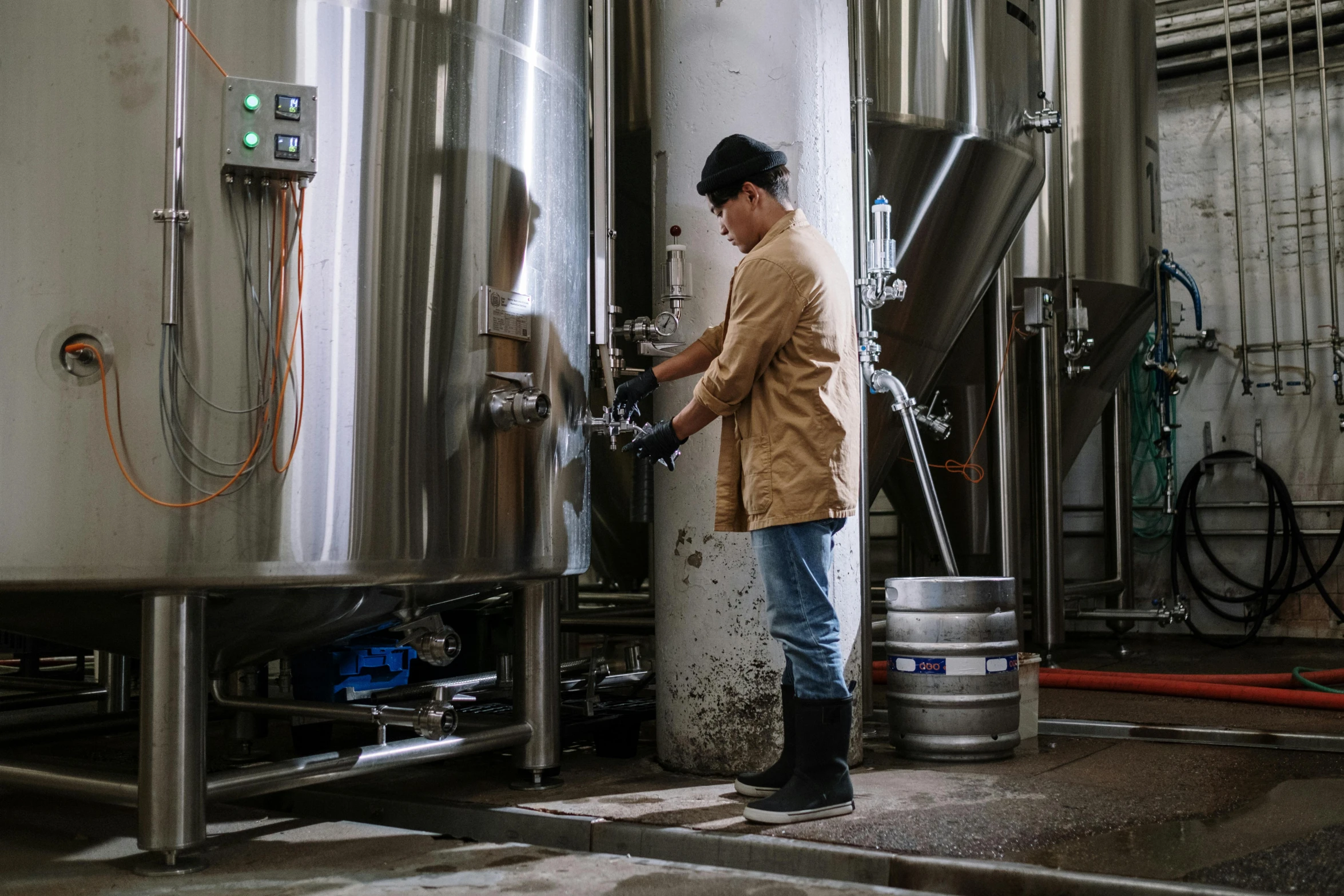 a man that is standing in front of a tank, by Tuvia Beeri, pexels contest winner, process art, holding the pint of ale, working, stainless steel, brown