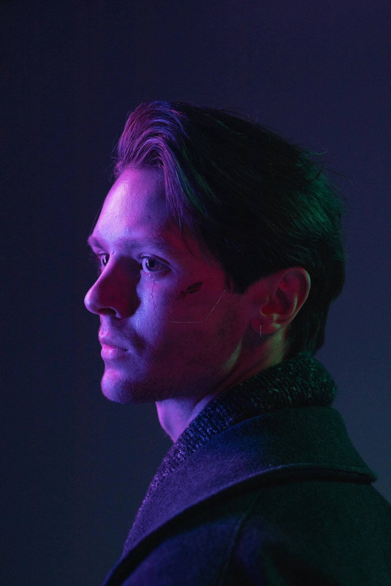 a man standing in front of a purple light, a character portrait, inspired by Julian Allen, pexels, bauhaus, with high cheekbones, facing away from camera, caleb from critical role, tobey maguire