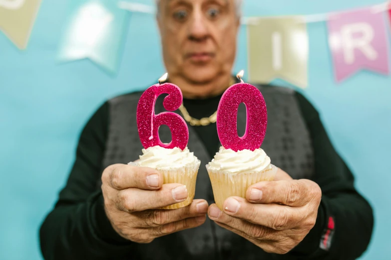 a man holding two cupcakes with candles on them, by Julia Pishtar, trending on unsplash, she is about 6 0 years old, pete davidson, 6, pink