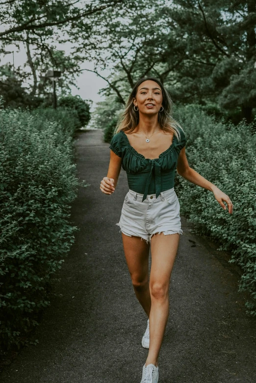 a woman in a green top and white shorts running down a path, pexels contest winner, pokimane, wearing denim short shorts, bare midriff, 2019 trending photo