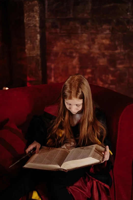 a girl sitting on a red couch reading a book, pexels contest winner, renaissance, spell casting wizard, aged 13, ellie bamber, illuminating the area
