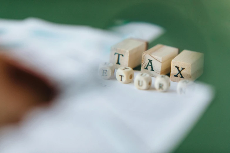 a person holding a piece of wood with the word tax spelled on it, a tilt shift photo, by Julian Allen, pexels contest winner, visual art, cubes on table, pastel', 1 6 x 1 6, small stature