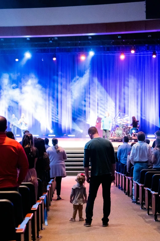 a group of people that are standing in front of a stage, worship, people walking around, in a sanctuary, spotlights