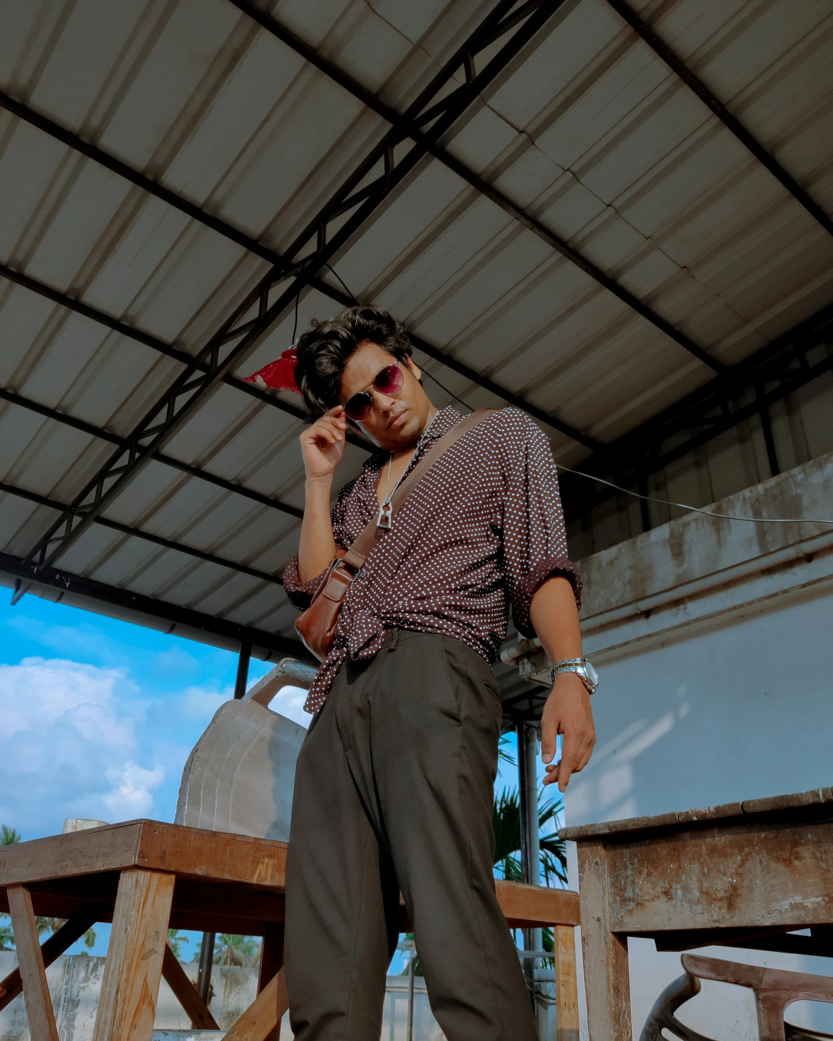 a man standing next to a table talking on a cell phone, an album cover, by Byron Galvez, unsplash, wearing shades, assamese aesthetic, androgynous person, standing on a rooftop