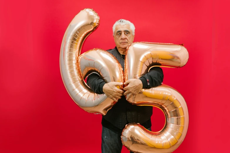 a man holding a large number balloon in front of a red background, by Edward Avedisian, pexels contest winner, 5 5 yo, reza afshar, frank gehry, celebrating a birthday