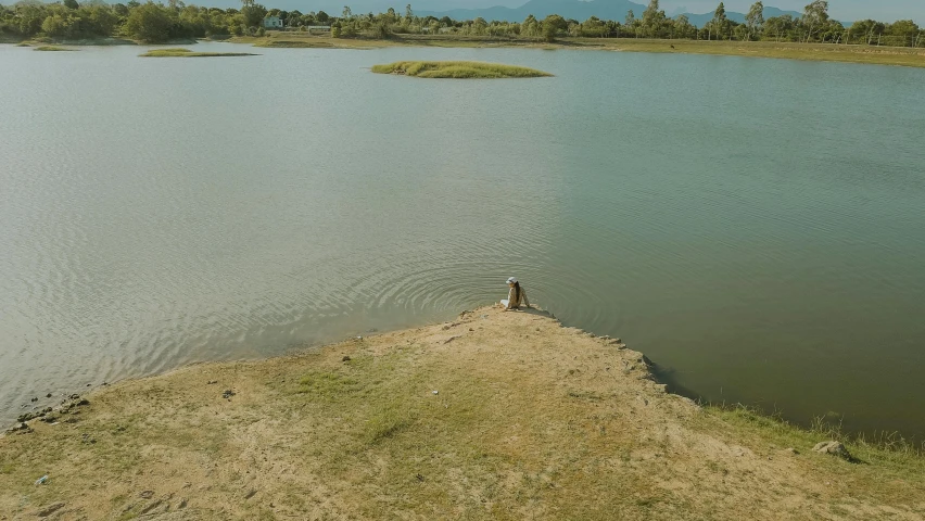 a person standing on the edge of a body of water, unsplash contest winner, land art, laos, wide high angle view, video still, sitting at a pond