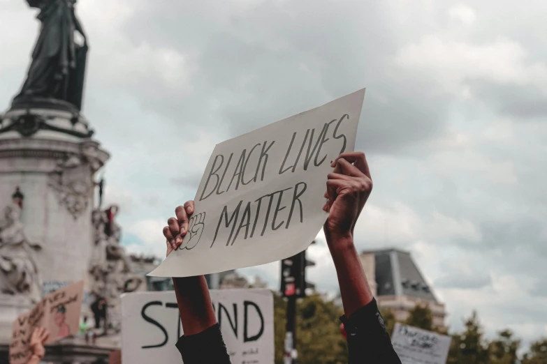 a person holding up a sign with a statue in the background, by Julia Pishtar, trending on pexels, black arts movement, background image, black canvas, low - angle shot, schools