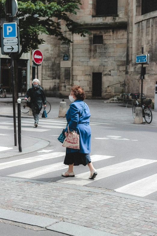 a woman in a blue coat crossing a street, les automatistes, slightly overweight, hot weather, older woman, high quality photo