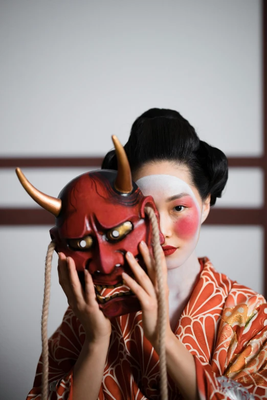 a woman holding a mask in front of her face, a picture, inspired by Shunkōsai Hokushū, trending on unsplash, human dressed as a bull, ( ( theatrical ) ), square, devil horns