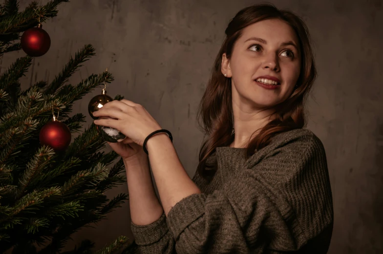 a woman decorating a christmas tree with ornaments, a portrait, by Julia Pishtar, pexels contest winner, dark. studio lighting, woman with braided brown hair, promotional image, holding gold watch