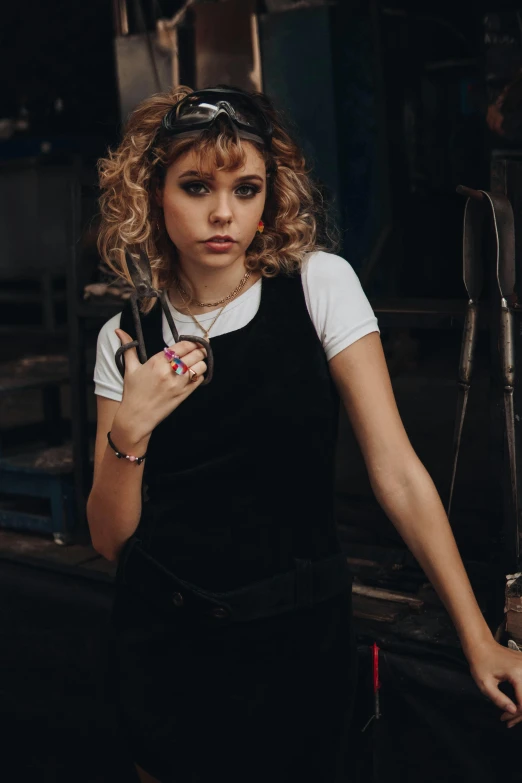 a woman standing in a kitchen holding a knife, trending on pexels, photorealism, mechanic punk outfit, short golden curls, grace moretz, woman in a dark factory