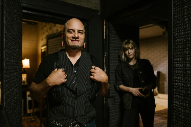 a man standing next to a woman in a room, a portrait, pexels contest winner, international gothic, philip selway (drums), back rooms, looking straight to camera, a man wearing a backpack