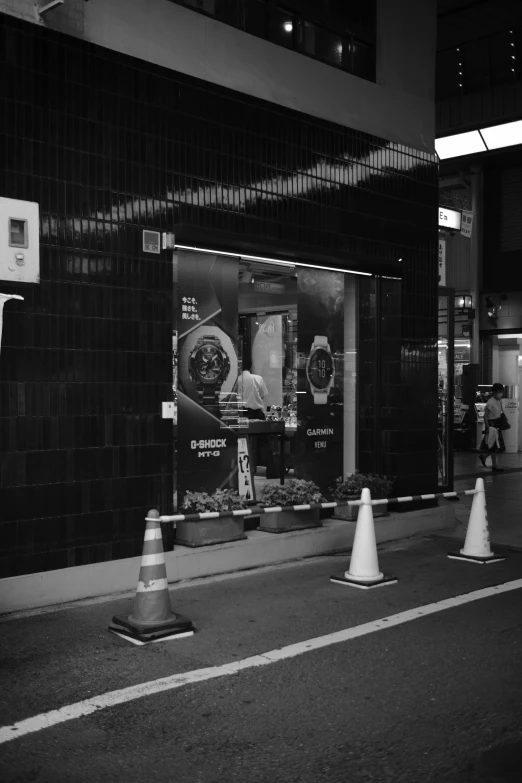 a couple of traffic cones sitting on the side of a road, a black and white photo, by Hirosada II, street art, night tokyo metropoly, shop front, hublot, security footage