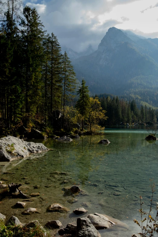 a body of water surrounded by trees and rocks, a picture, by Sebastian Spreng, dolomites in background, sad look, no cropping, serene forest setting